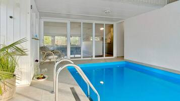 An indoor swimming pool with a clear view of the adjacent room, a chair, and a potted plant.