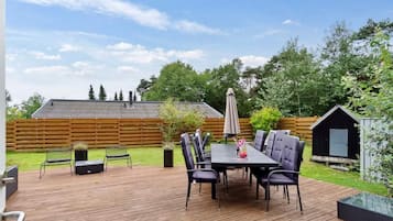 A wooden deck with a table and chairs, a small shed, and a fenced yard.