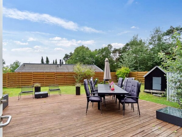 A wooden deck with a table and chairs, a small shed, and a fenced yard.