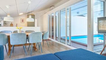 A modern dining area with a pool view, featuring a table with chairs, a sofa, and a TV.