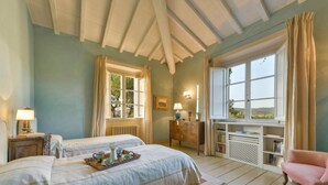 A bedroom with two beds, a dresser, a window with a view, and a pink chair. - Luxury villa at 15 minutes driving from the seaside (Gavorrano)