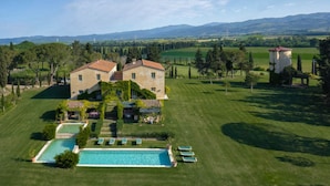 Una casa grande con piscina, rodeada de césped cuidado y árboles.