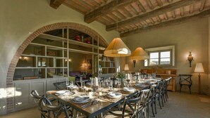 Un comedor con una mesa larga dispuesta para una comida, arcos de ladrillo y un techo alto con vigas a la vista.