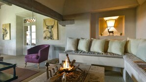 Una sala de estar acogedora con chimenea, un sillón púrpura, un sofá con varios cojines y cuadros con representaciones de animales.