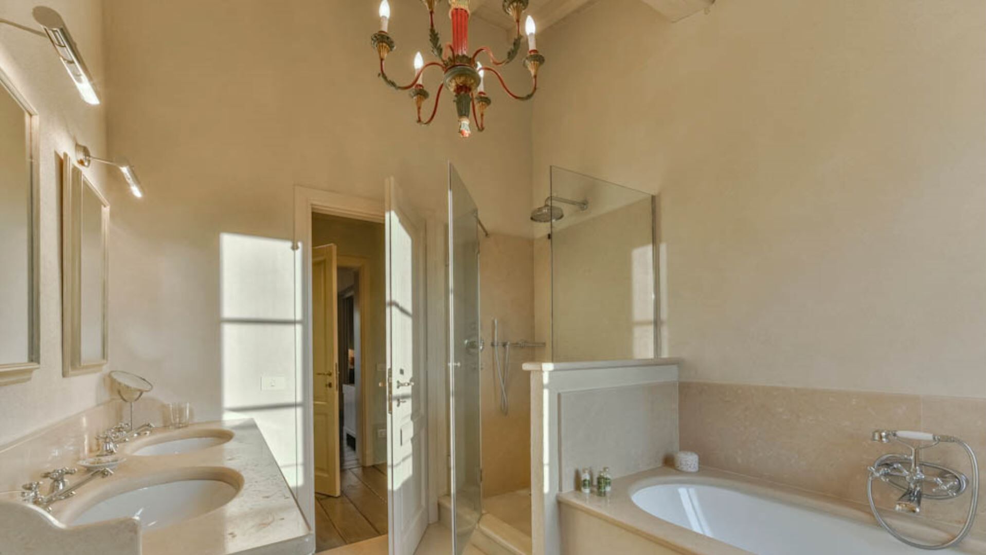 Une salle de bain spacieuse avec deux lavabos, une baignoire, une douche et un lustre.