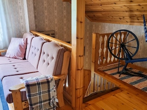 A cozy cabin interior with a wooden bed, a plaid blanket, and a spinning wheel.