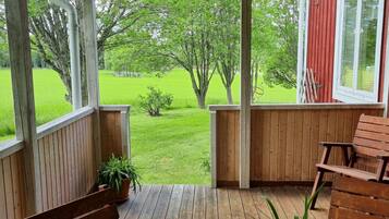 A wooden deck with a bench and a table, overlooking a green lawn and trees.