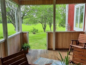 Une terrasse en bois avec un banc et une table, donnant sur une pelouse verdoyante et des arbres.