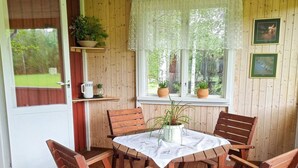 A wooden deck with a round table and four chairs, surrounded by potted plants and framed pictures on the walls. - 4 Person Holiday Home in Jarvso (Jarvso)