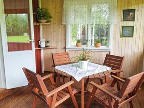 A wooden deck with a round table and four chairs, surrounded by potted plants and framed pictures on the walls. - 4 Person Holiday Home in Jarvso (Jarvso)