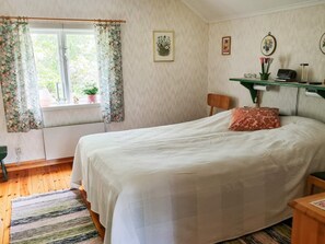 A bedroom with a bed, a window with floral curtains, a desk with a printer, and a shelf with decorative items. - 4 Person Holiday Home in Jarvso (Jarvso)