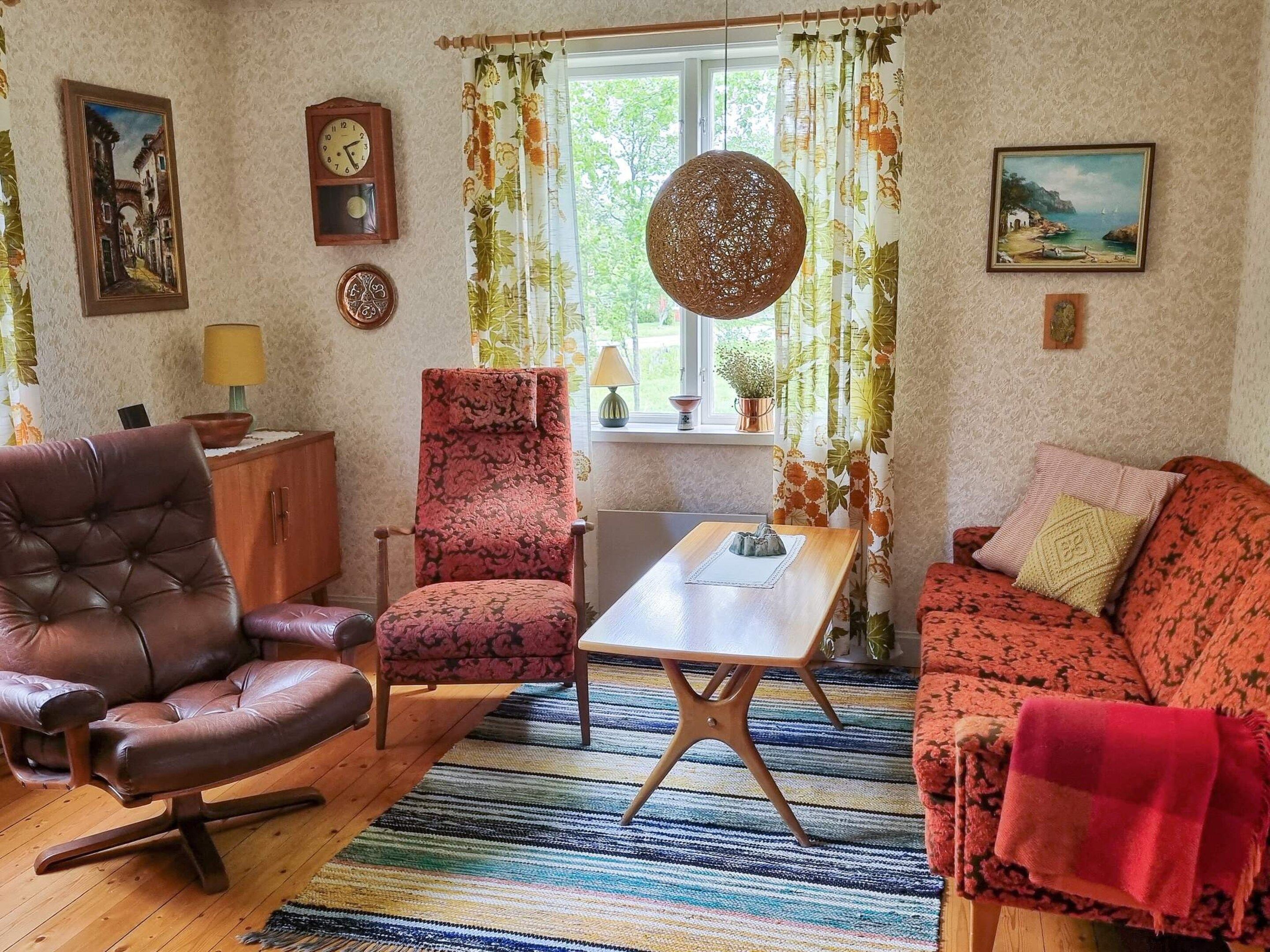 A cozy living room with a leather armchair, a patterned armchair, a sofa, a wooden coffee table, and a large window with curtains.