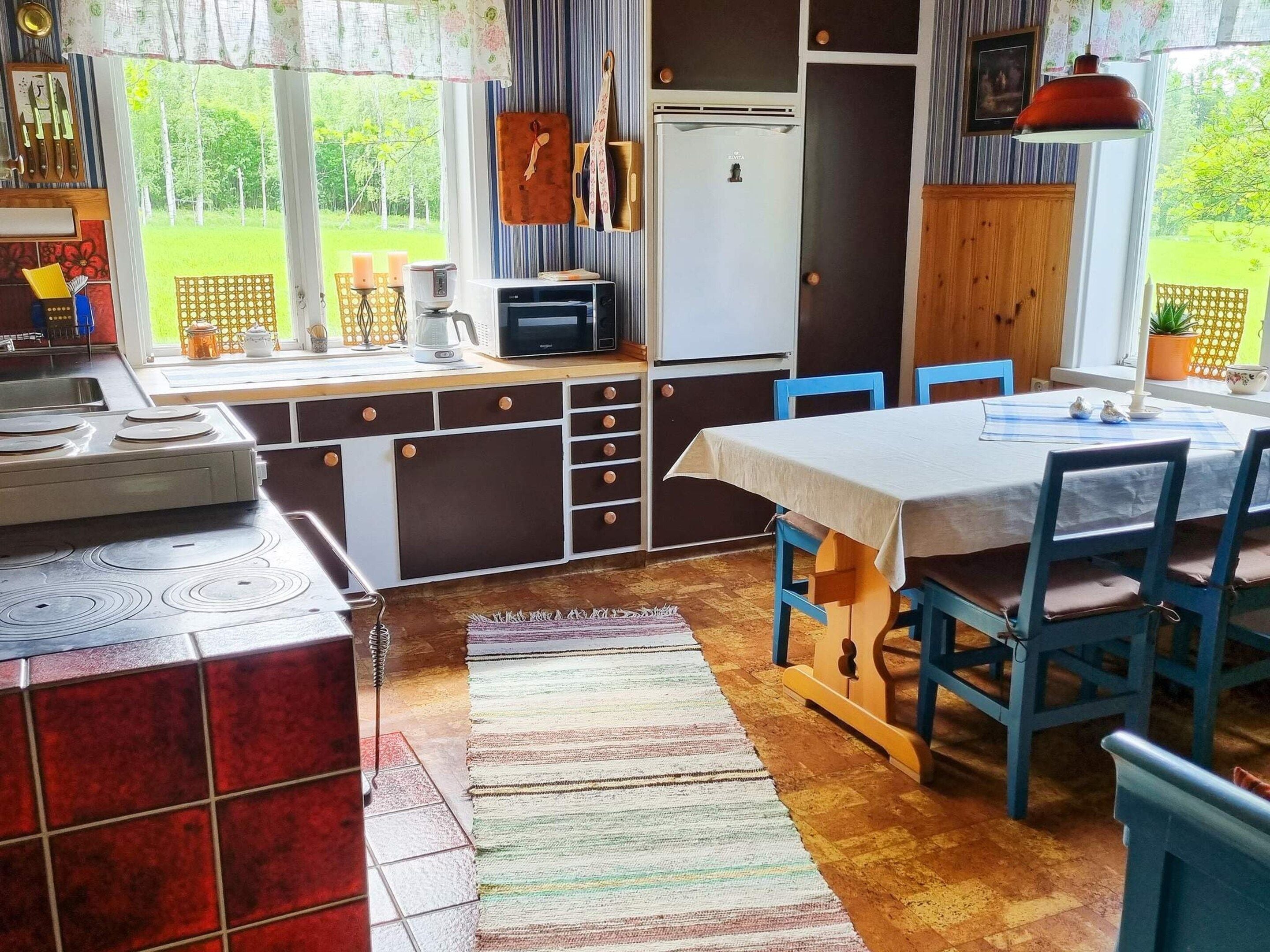 Een keuken met een eethoek, een koelkast en een raam met uitzicht op groen.