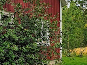 Une grange rouge avec une porte blanche, entourée d’un feuillage vert et dense.