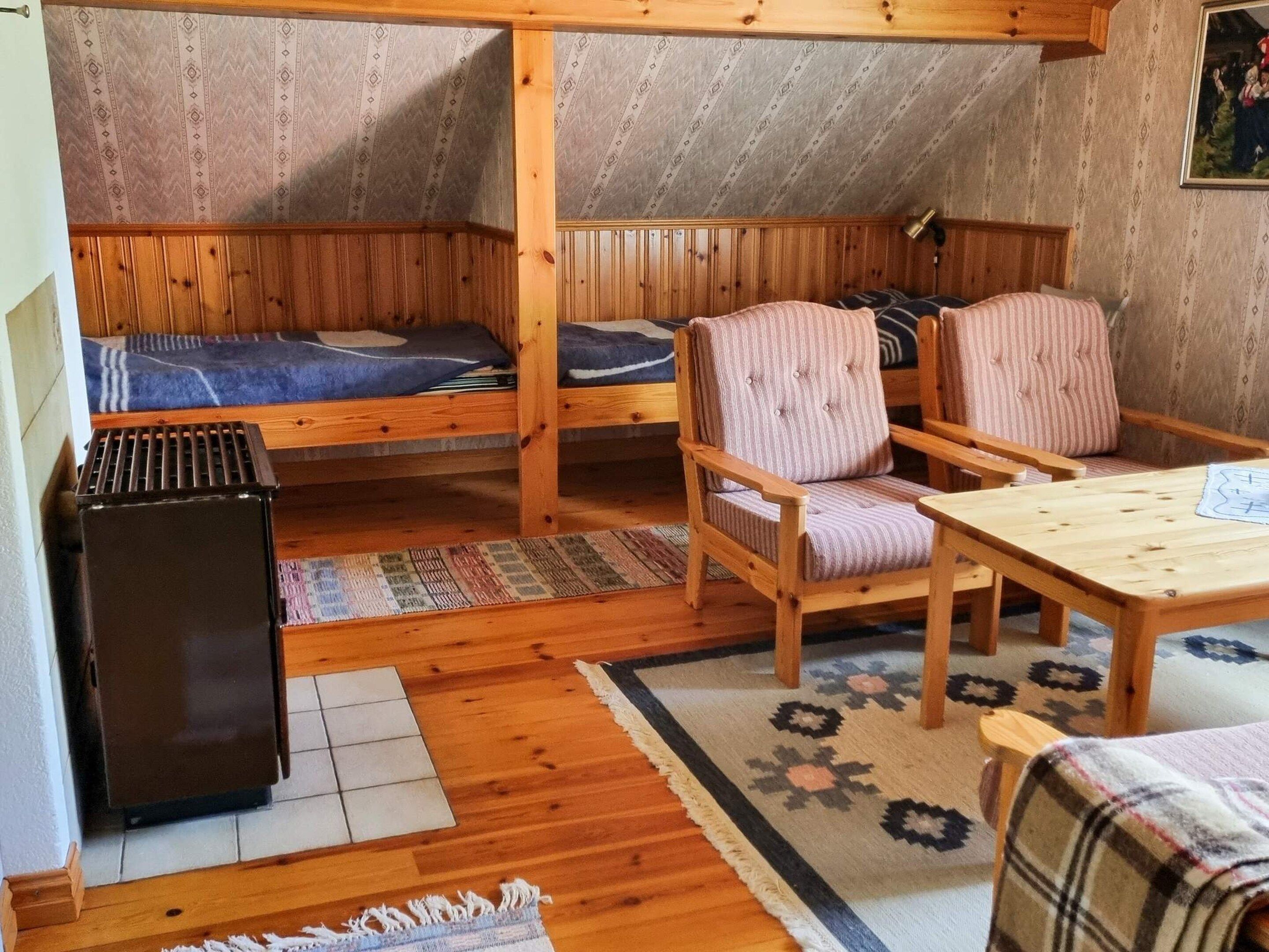 A cozy room with two bunk beds, a small table, two chairs, a radiator, and a patterned rug.