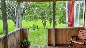 A wooden porch with a view of a green lawn and trees.