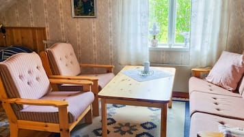 A cozy room with a wooden floor, a patterned rug, a table with a candle, and a window with curtains.