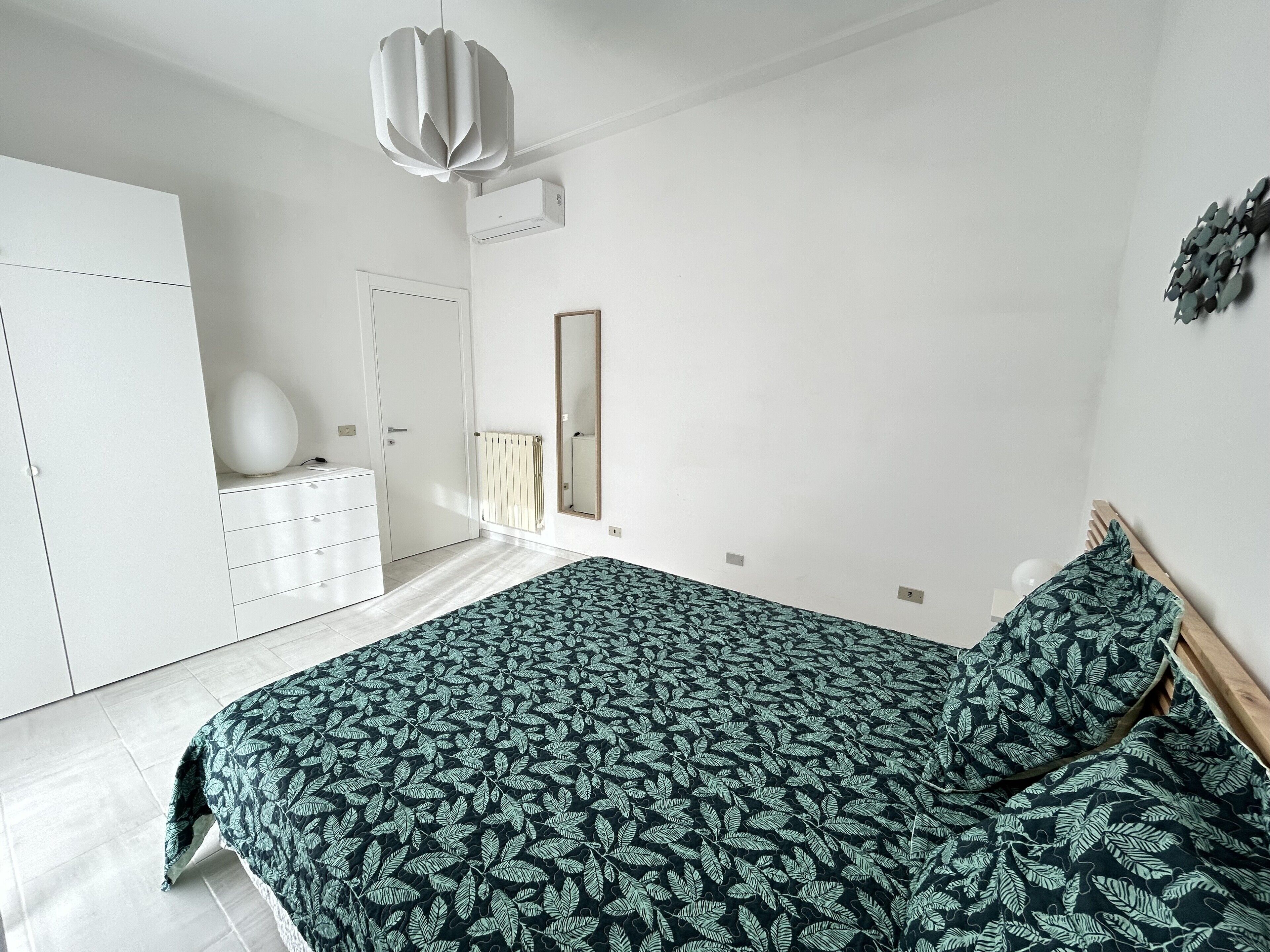 Une chambre à coucher comprenant un lit, une commode, une armoire et un luminaire suspendu.
