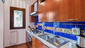 A kitchen with wooden cabinets, a gas stove, two sinks, and colorful backsplash tiles. - Marquis-Taormina holiday home (Taormina)