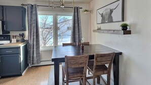 A modern kitchen with dark cabinets, a wooden dining table, and a chandelier.