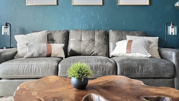 A living room with a grey sectional sofa, three framed black and white photographs on the wall, a small potted plant on a wooden coffee table, and two floor lamps on either side of the sofa.