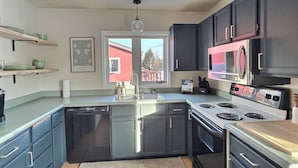 A modern kitchen with dark cabinets, stainless steel appliances, and a window providing a view of the outside.