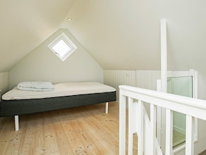 Une chambre avec un plafond en pente, un lit simple, une petite fenêtre et un plancher en bois.
