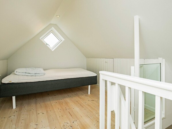 A bedroom with a sloped ceiling, a single bed, a small window, and a wooden floor.