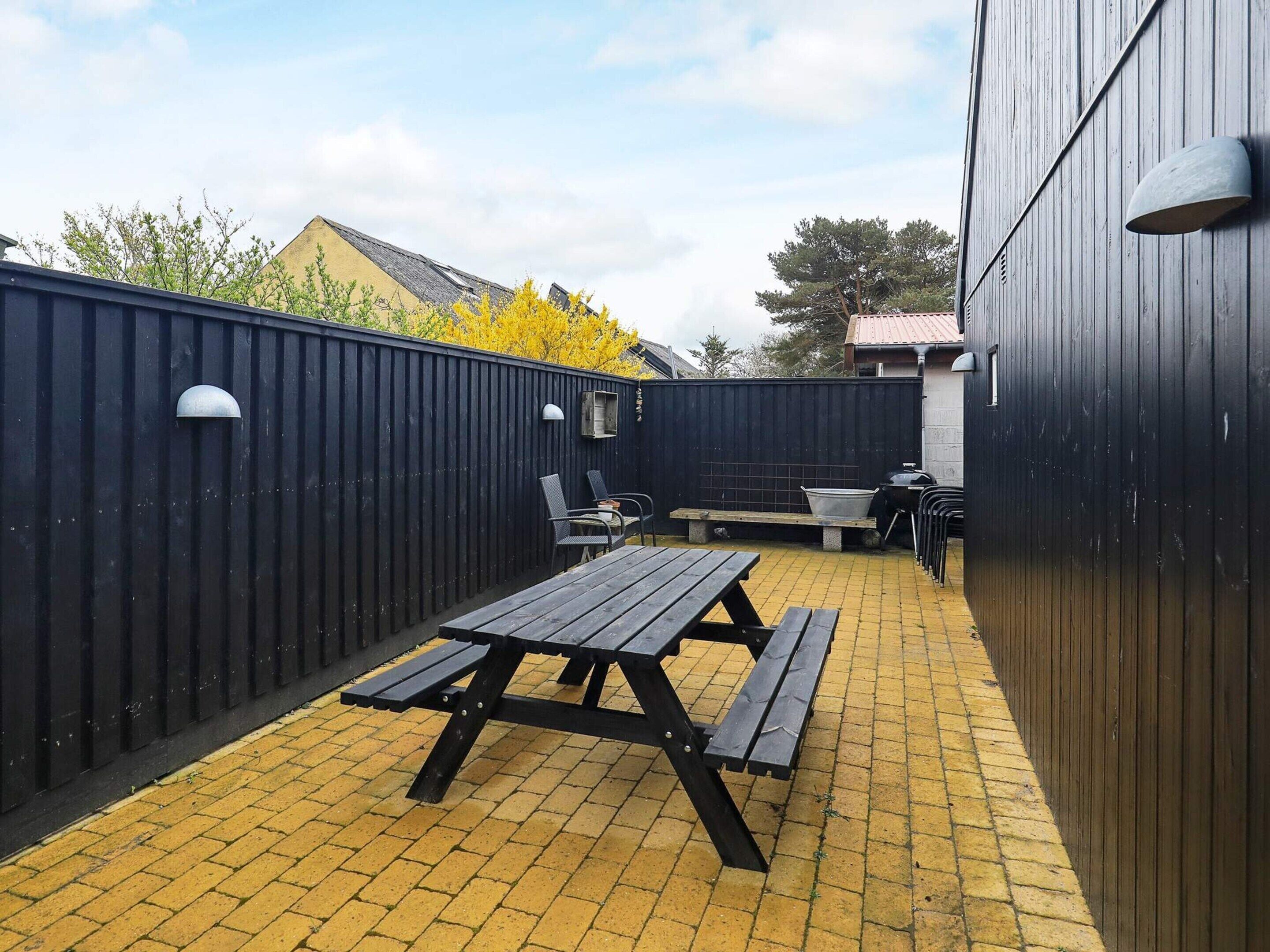 A patio area with a picnic table and chairs, a barbecue grill, and a fenced enclosure.