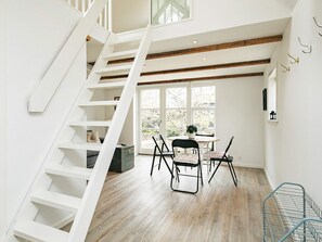 Une pièce spacieuse avec un plancher en bois, un escalier blanc et un coin repas comprenant des chaises et une table.