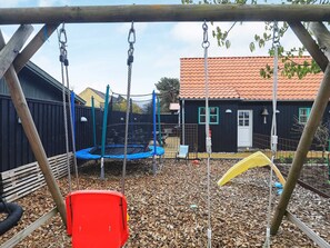 A playground with a swing set, a trampoline, and a yellow slide. - 4 Star Holiday Home in Skagen (Skagen)