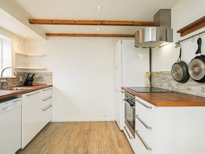 A kitchen with white cabinetry, wooden beams, a stainless steel range hood, and a hanging pot rack. - 4 Star Holiday Home in Skagen (Skagen)