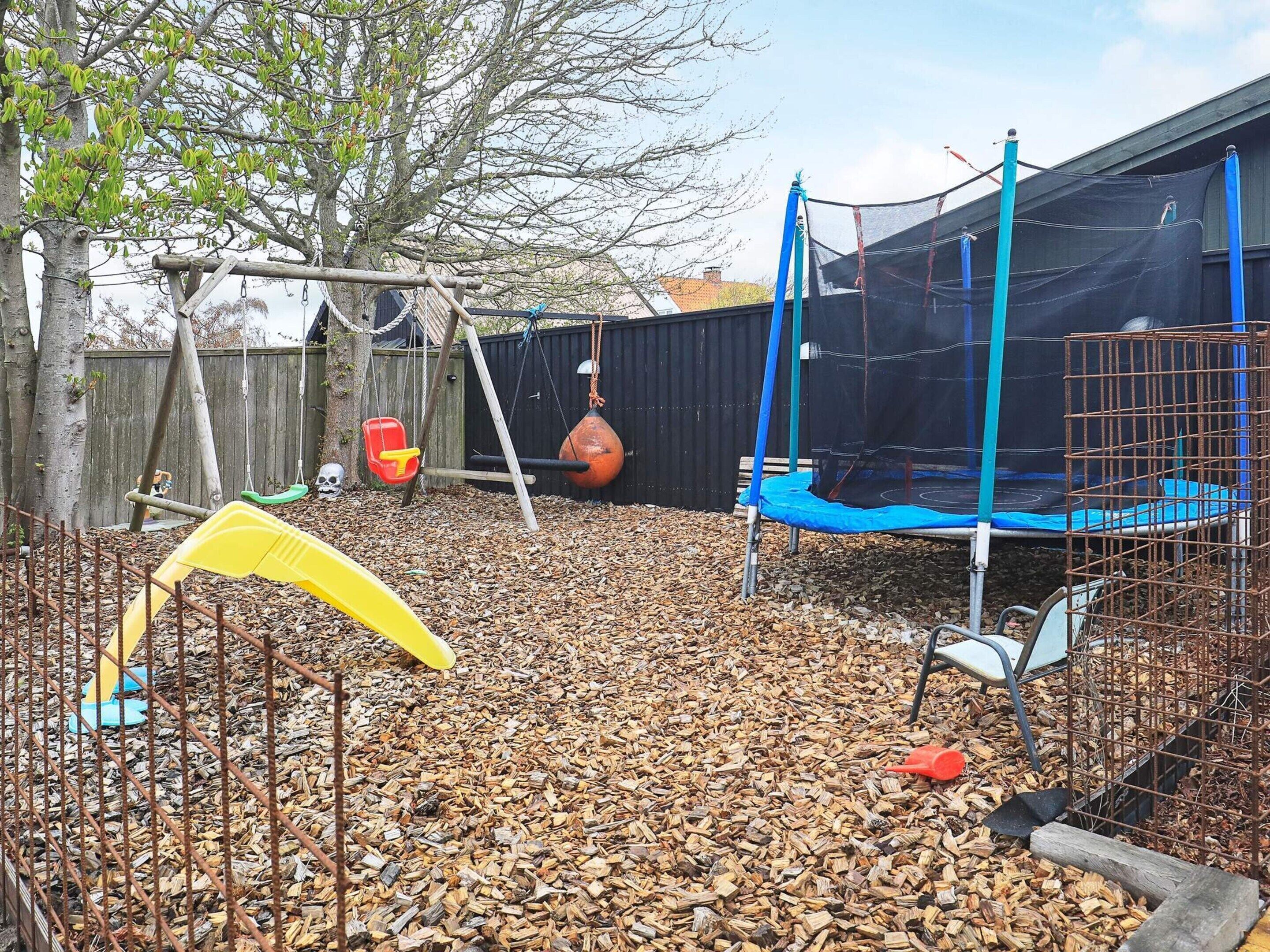A backyard with a trampoline, swing set, and a yellow play structure.