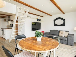 A modern living room with a wooden dining table, a gray sofa, a TV mounted on the wall, and a wooden ceiling with exposed beams. - 4 Star Holiday Home in Skagen (Skagen)