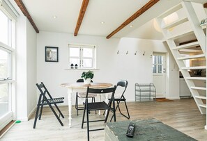 A dining area with a round table, chairs, and a plant. There is a staircase with a white railing and a door leading to another room.