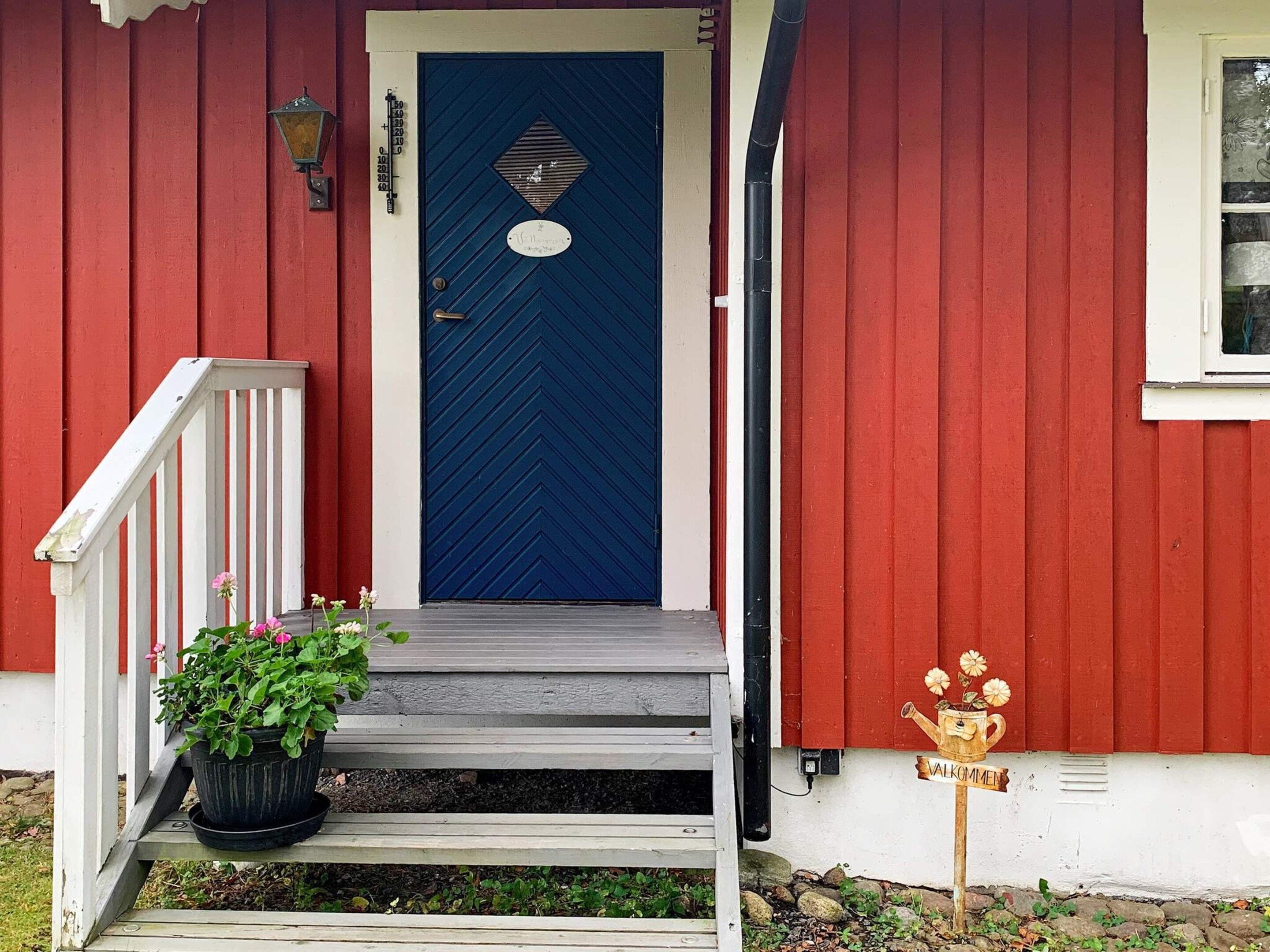 A red house with a blue door, a small porch with steps, and a potted plant.
