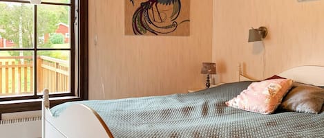 Un dormitorio con cama, ventana, lámpara de pared y un cuadro.