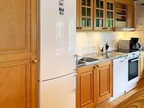 A kitchen with wooden cabinets, a white refrigerator, a double sink, and a coffee maker. - 4 Person Holiday Home in Holsljunga (Holsljunga)