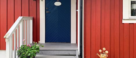 A red house with a blue door, a white porch, and a potted plant.