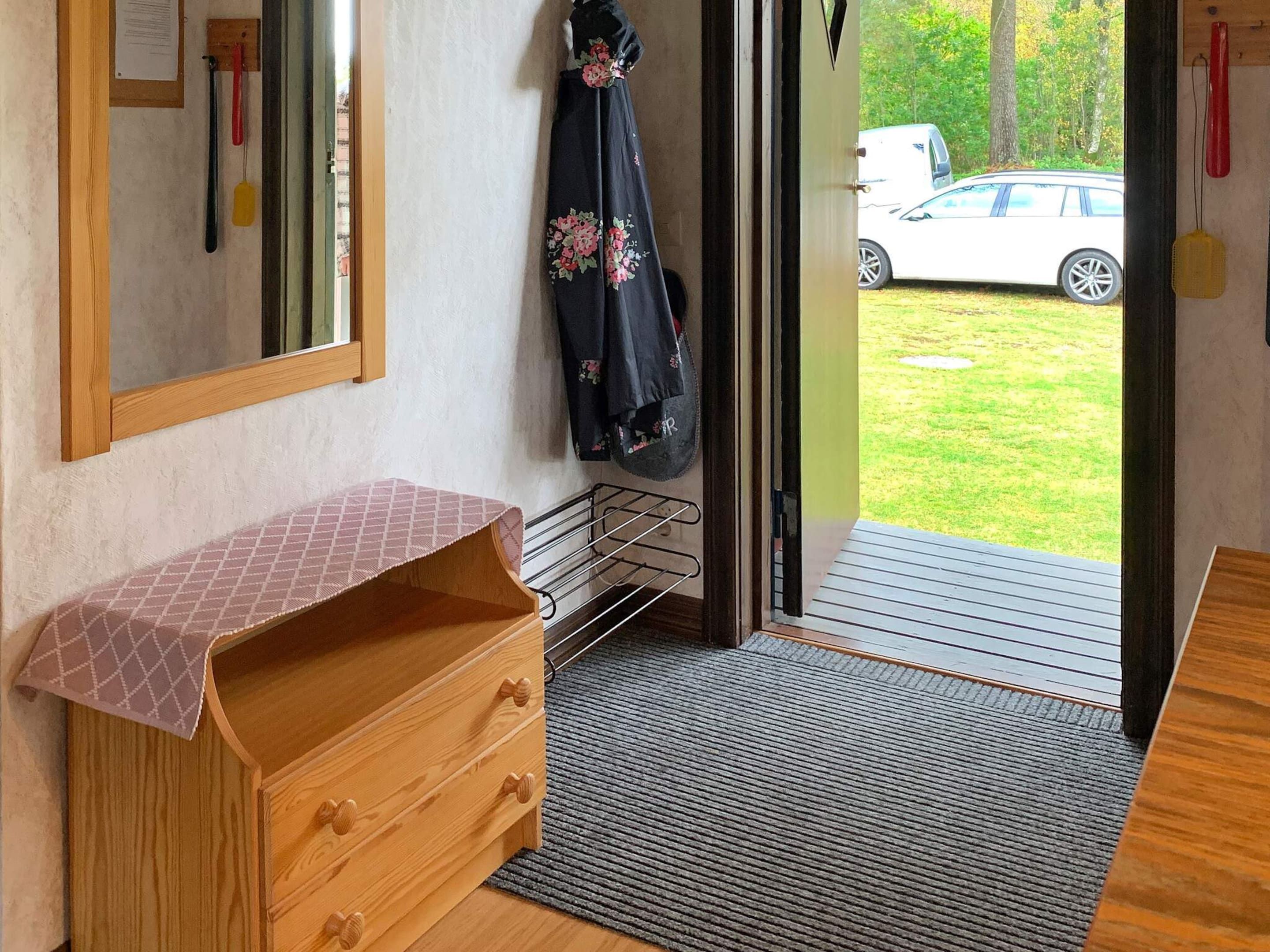 A room with a wooden dresser, a mirror, a coat rack with a floral garment, and a view of a white car through an open door.