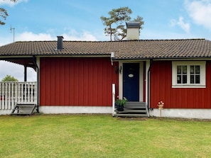 A red building with a tiled roof, a blue door, and a small porch with steps. - 4 Person Holiday Home in Holsljunga (Holsljunga)