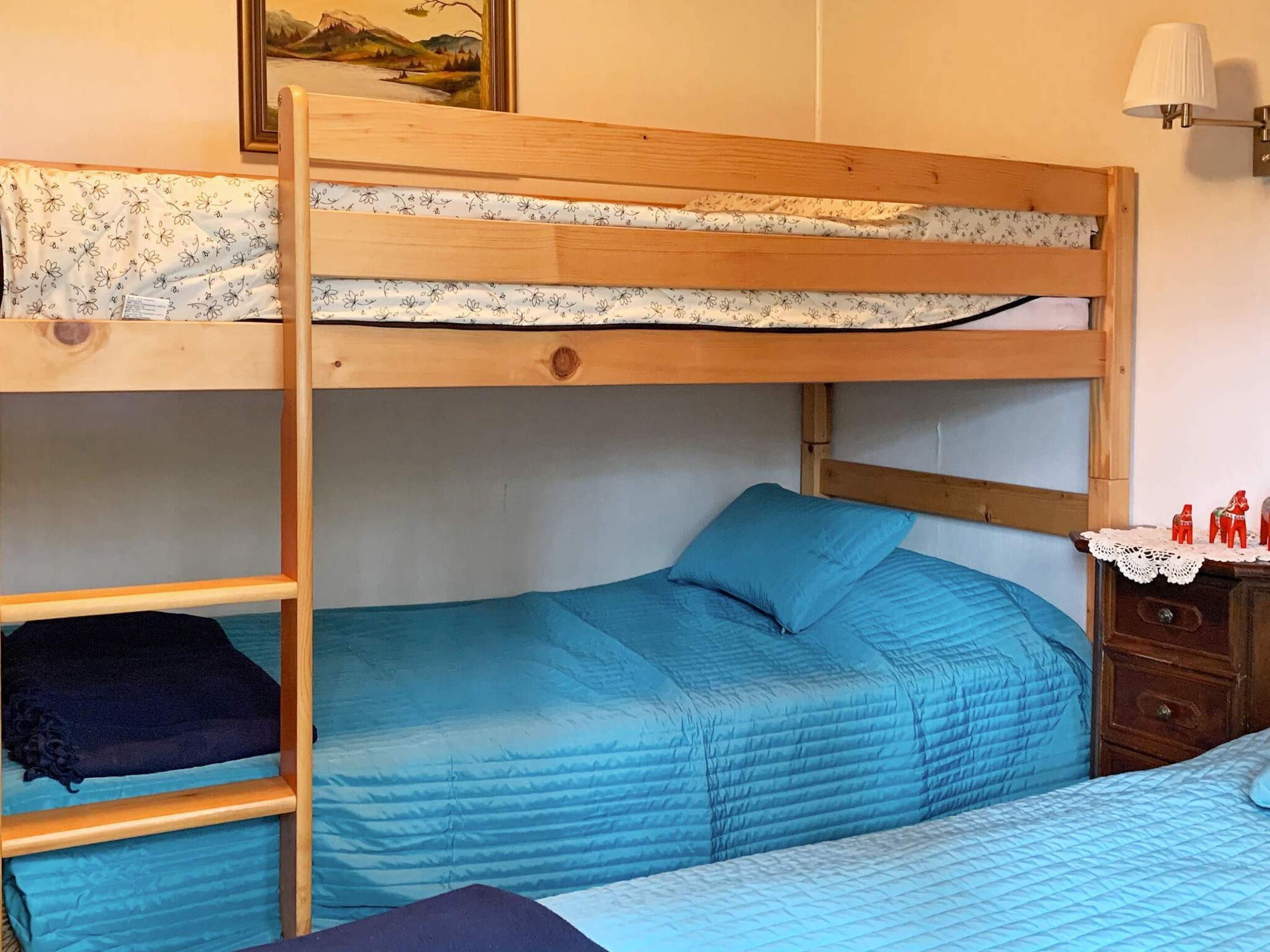 A bunk bed with a lower bunk, a blue bedspread, and a wooden ladder.