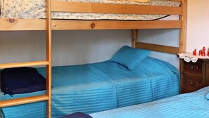 Un lit superposé avec un lit inférieur, une couverture bleue et une échelle en bois.