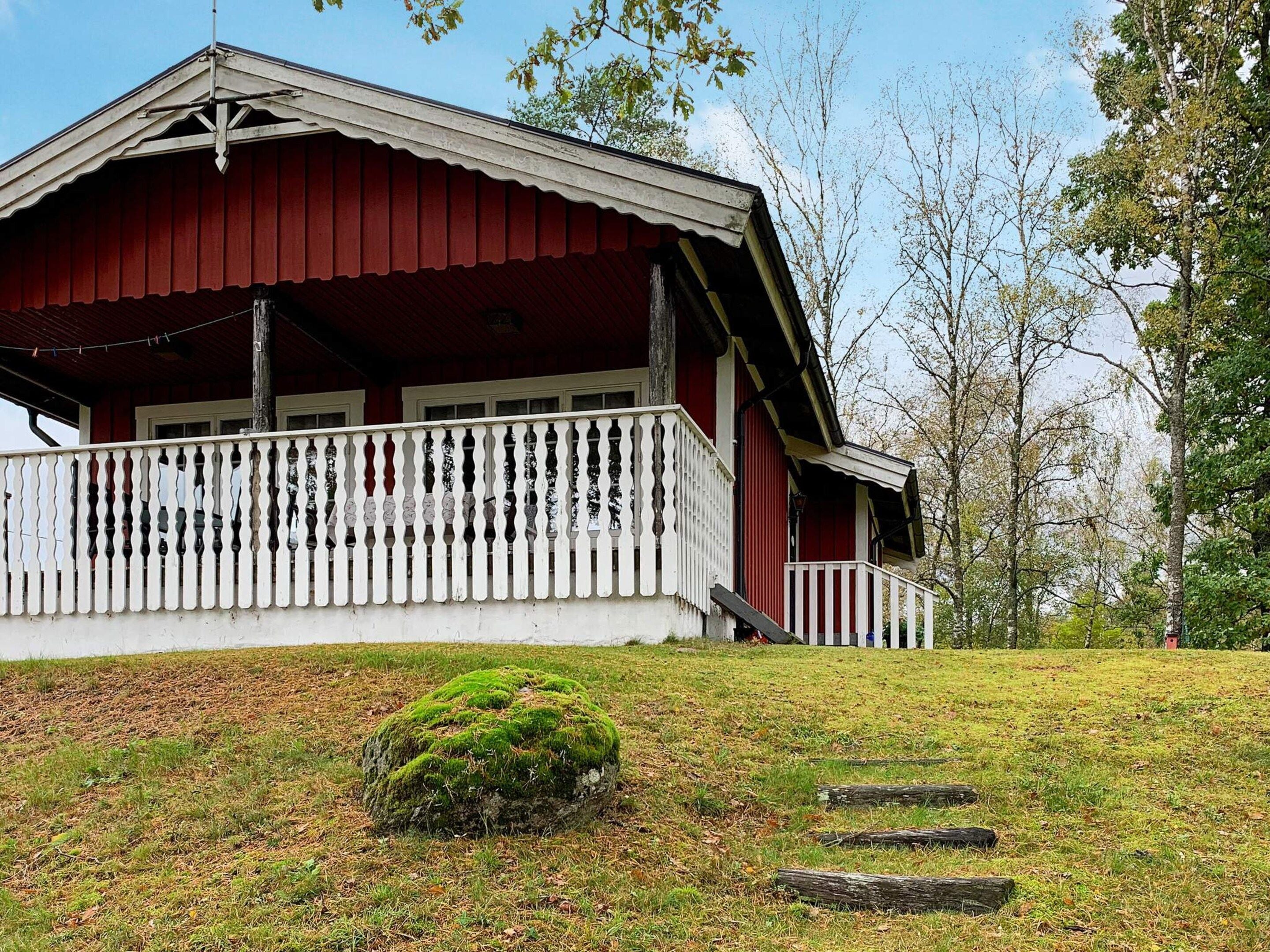 A red wooden house with a white porch and a small green bush in front.