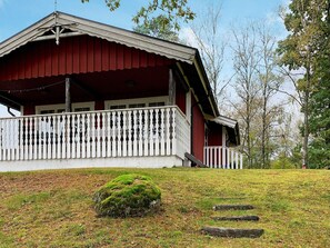 Une maison en bois rouge, avec un porche blanc et un petit arbuste vert devant.