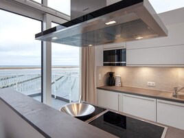 Cocina moderna con vista al mar, campana extractora de acero inoxidable, microondas y horno empotrado.