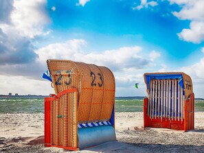 Two beach huts with numbers 23 and 24, a sandy beach, and a body of water in the background.