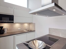 Una cocina moderna con microondas integrado, un lavamanos de acero inoxidable y una estufa con una sartén.