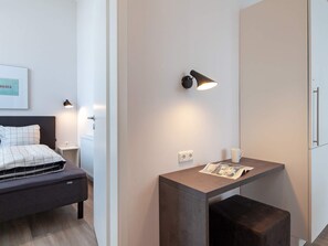 A modern hotel room with a bed, bedside table, lamp, and a small desk with a magazine.