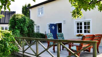 A wooden deck with a table and chairs, a blue door, and a white building with windows.